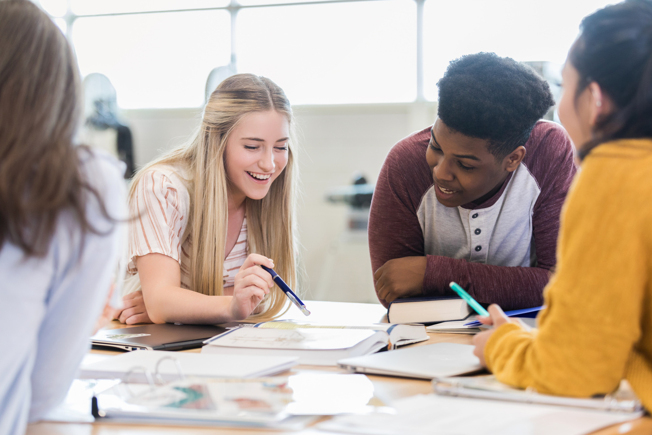 Teen girl reads textbook with classmates